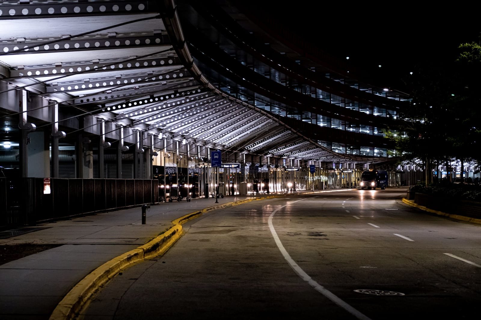 Airport terminal kerbside at night, lit canopy curving away above an empty drop-off lane